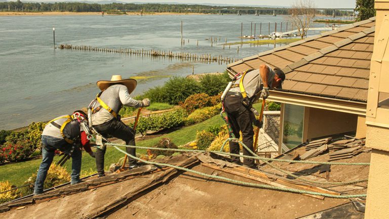 Two Cherry Roofing crew members working on the roof of a home by the water.